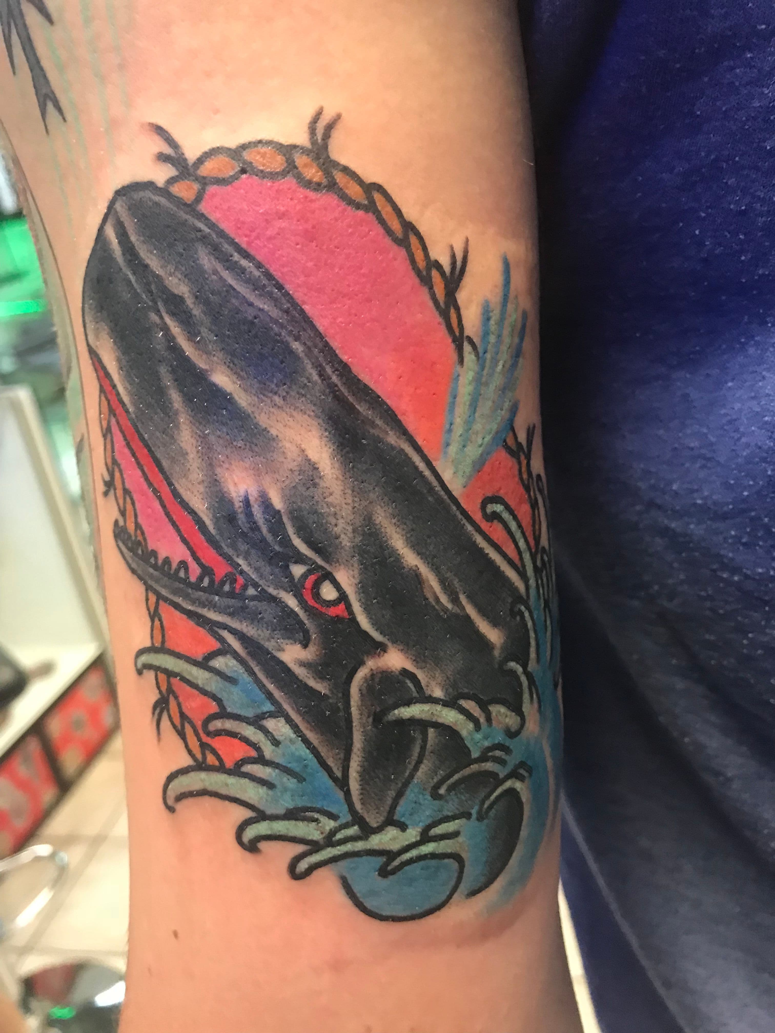 Colorful tattoo of a whale and waves on a forearm