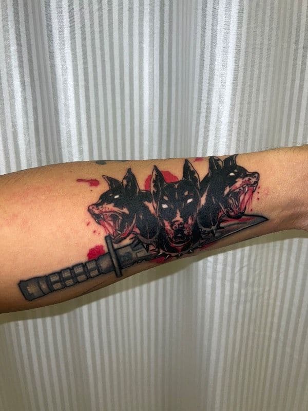 Tattoo of a three-headed dog with sword on forearm