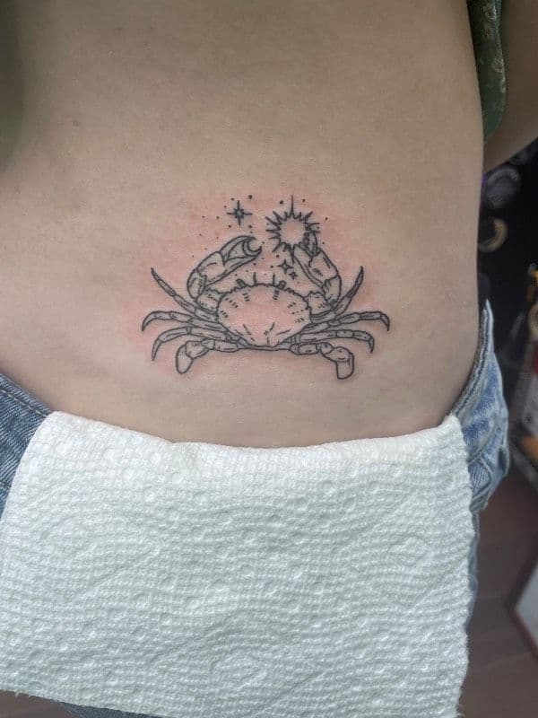 Tattoo of a crab with celestial symbols on the torso.