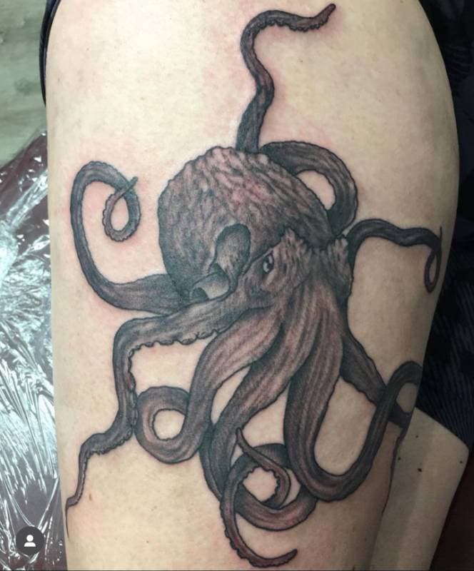 Black and grey tattoo of an octopus on the thigh.